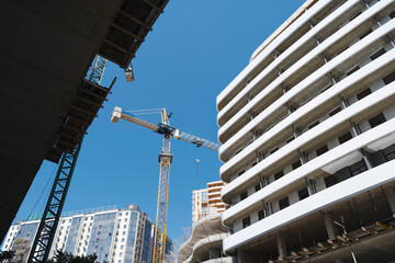 A low-angle shot of a construction site with a towering yellow crane and modern buildings under a...