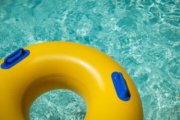 Bright yellow inflatable ring floating in a clear blue lazy river surrounded by lush greenery. A...