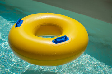 Bright yellow inflatable ring floating in a clear blue lazy river surrounded by lush greenery. A...