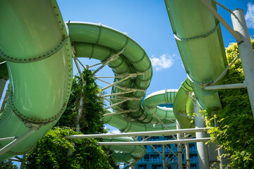 View from below of a green water slide structure in a modern aqua park, surrounded by lush greenery...