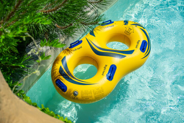 Bright yellow inflatable ring floating in a clear blue lazy river surrounded by lush greenery. A...