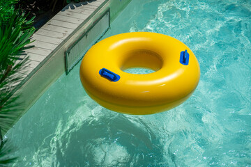 Bright yellow inflatable ring floating in a clear blue lazy river surrounded by lush greenery. A...
