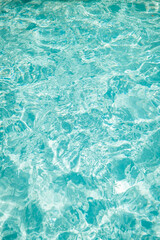 Bright sunlight creates shimmering patterns on the clear, turquoise water surface of a pool, evoking a refreshing and relaxing summer atmosphere.