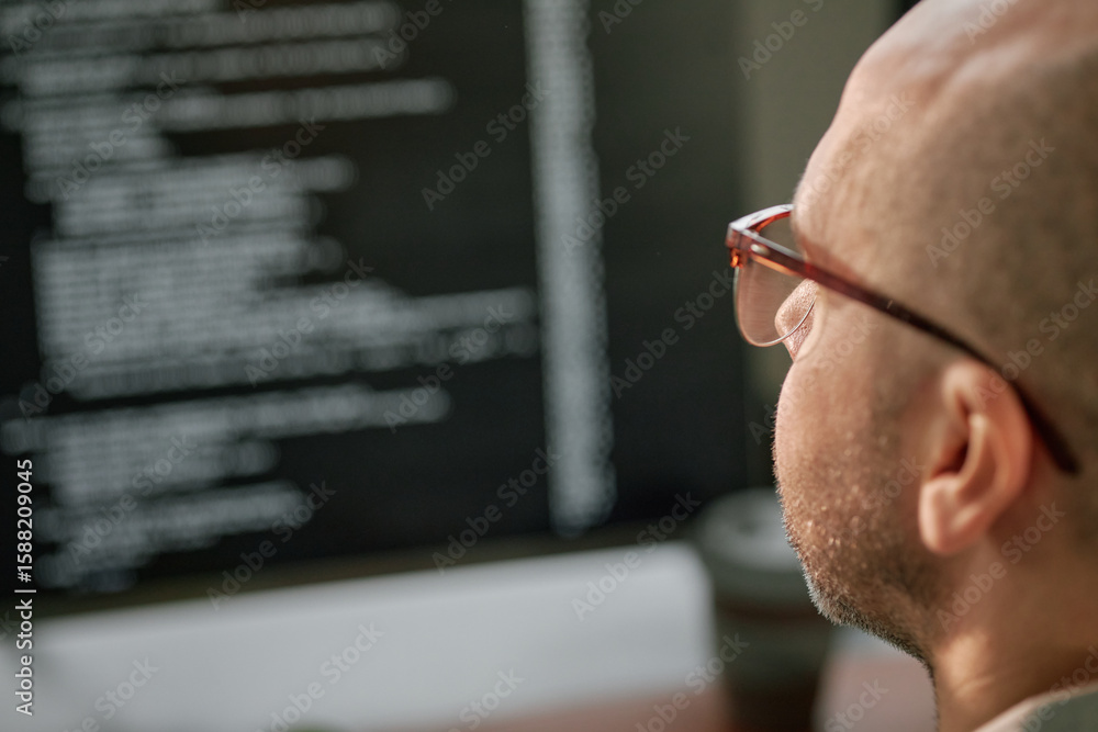 Poster caucasian middle aged man wearing glasses working on computer monitor displaying lines of code, sitt