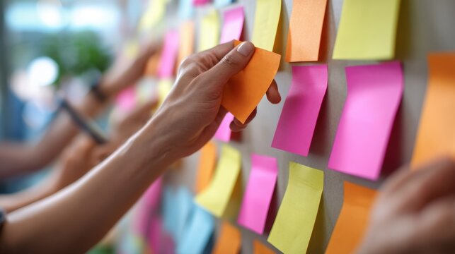 A person organizes colorful sticky notes on a board, likely during a brainstorming or planning session in a collaborative workspace.