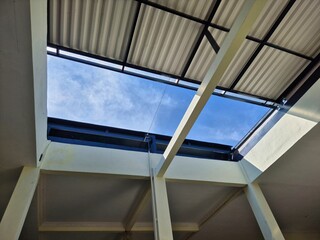 Fototapeta premium Open skylight in metal roof structure revealing blue sky and light clouds above