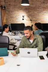Focused employee working on laptop and smartphone in modern office