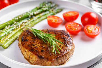 Close up, macro of tasty grilled beef steak served with green asparagus and cherry tomatoes on white plate, with cutlery. Perfect for food menu, diet, or culinary design concepts.