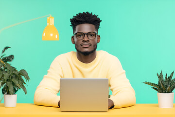Focused young man working on laptop at colorful desk with modern decor and indoor plants

