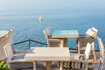 Seafront cafe terrace with wicker furniture and pillows overlooking calm water in Kotor Bay, Montenegro