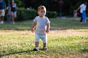 Toddler walking in park with pacifier, enjoying summer day