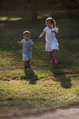 Two happy children running on grass in a park during sunset
