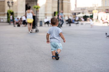 Toddler walking away in city square leaving parents behind