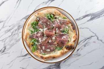 A top down view of a prosciutto and arugula pizza.