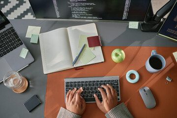 Young adult Black woman typing on wireless keyboard at modern workspace with open notebook, laptop,...