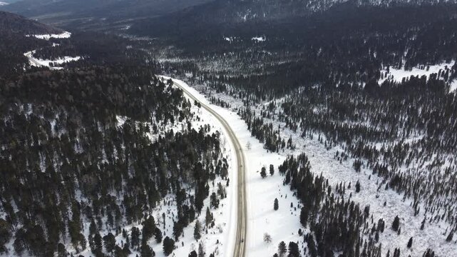 Aerial footage of a winding snow-covered road leading to Ust-Koksa in the Altai Republic, Russia. The video shows scenic winter landscapes with forests, hill