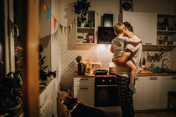 dad holds son in his arms and cooks at the stove in the kitchen in the evening