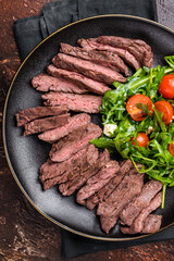 Grilled and sliced Beef Denver strip Steak on a plate with salad. brown background. top view