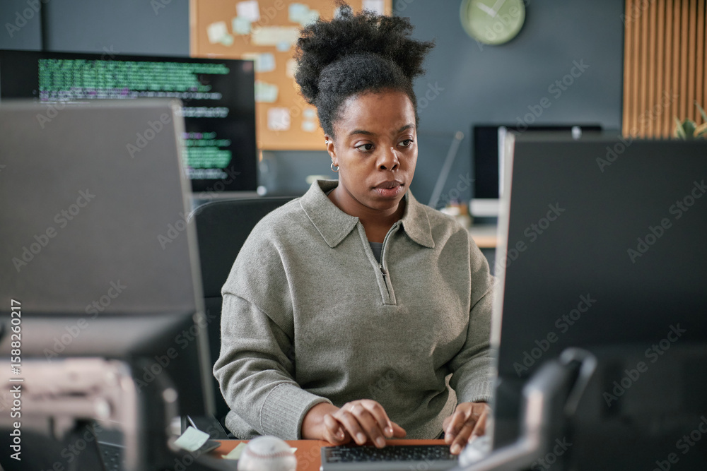 Poster black young adult woman working at computer desk, focusing on screen while typing on keyboard, surro