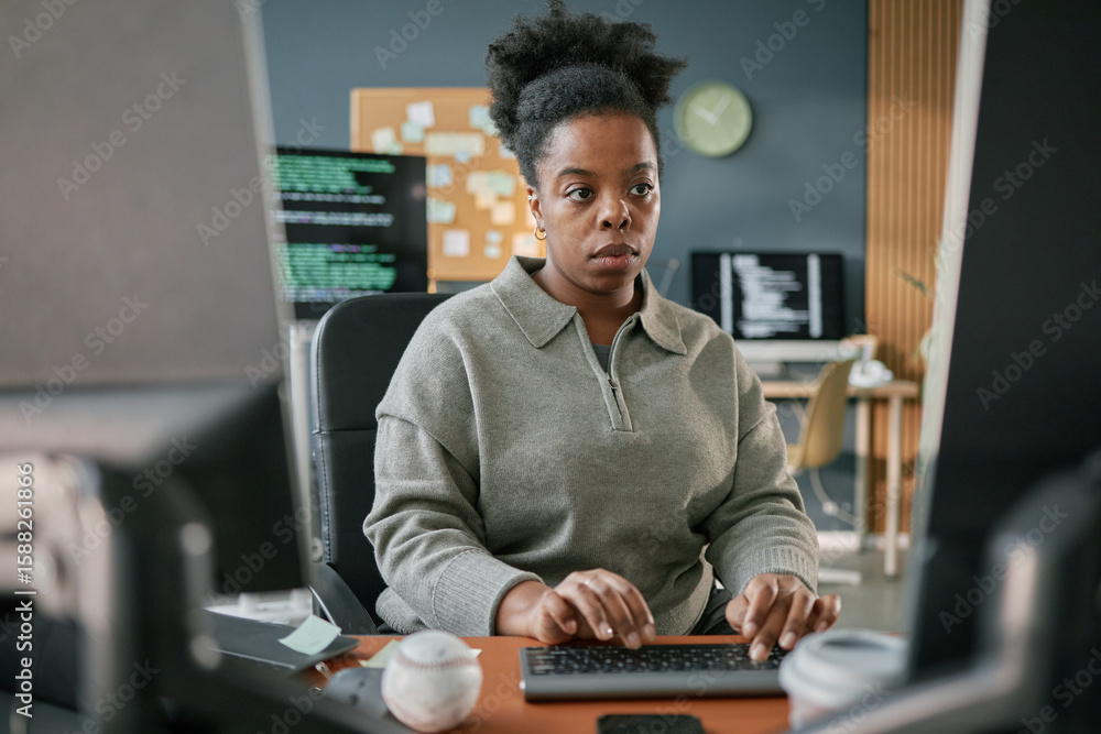 Poster young adult black woman working at computer desk, focusing on typing with hands on keyboard, sitting