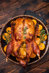Roast goose with apples and oranges on plate with herbs. wooden background. top view
