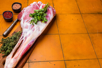 Whole raw lamb leg, uncooked mutton meat on butcher board. orange background. top view
