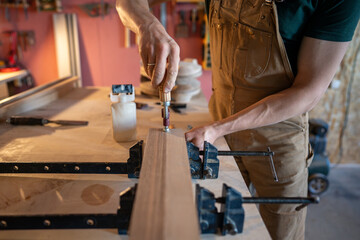 Carpenter hands tighten clamps with screwdriver to bind glued beams for large wooden board for...