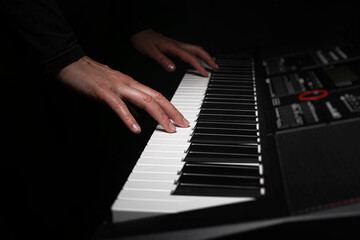 A pair of hands with long slender fingers gently presses down on the white keys of a digital piano...