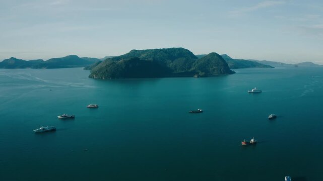 March 11th, 2022 - Langkawi, Malaysia: 4k Establishing b-roll aerial shot of drone moving forward over the deep blue sea towards Pulau Tuba island. High angle view of scattered passenger ferries, carg