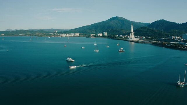 March 11th, 2022 - Langkawi, Malaysia: 4k Establishing b-roll aerial shot of drone rising and moving forward over the blue waters of Kuah bay towards the waterfront skyline. Tower landmark, lush mount