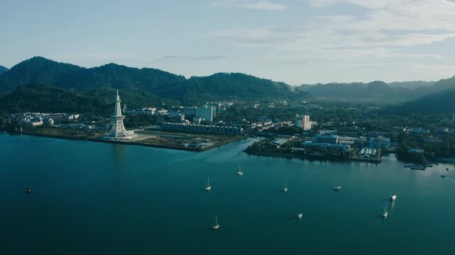 March 11th, 2022 - Langkawi, Malaysia: 4k Establishing b-roll aerial shot of drone moving forward over the calm blue sea toward Kuah town waterfront. Panoramic view of the tower landmark, coastal buil