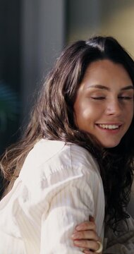 A young woman smiles at the camera. She's sitting at her desk in the office. An open laptop on the table in front of her