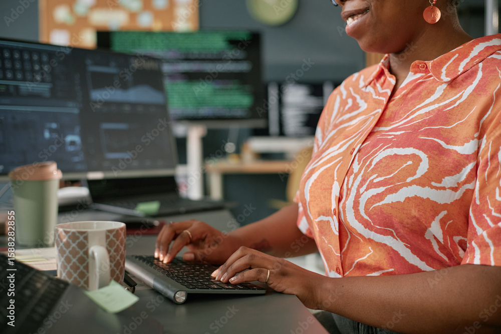 Poster young adult black woman working at computer desk, typing on wireless keyboard with multiple monitors