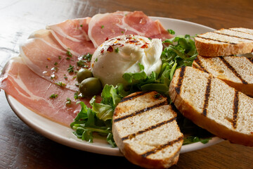 A view of a plate of burrata and prosciutto.