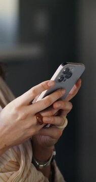 A woman uses a mobile phone while working in an office. Close-up of her hands, unrecognizable person