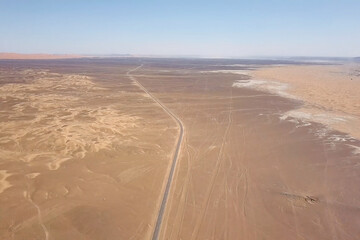 Aerial view reveals a vast desert landscape with an arid wilderness stretching towards the horizon, intersected by a winding road