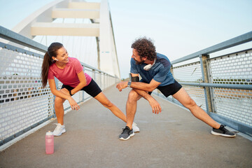 Two individuals are performing stretching exercises on a bridge while enjoying a morning workout together. Their activity encourages a recreational and healthy lifestyle.