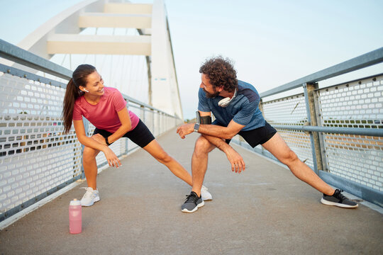 Two individuals are performing stretching exercises on a bridge while enjoying a morning workout together. Their activity encourages a recreational and healthy lifestyle. - Powered by Adobe