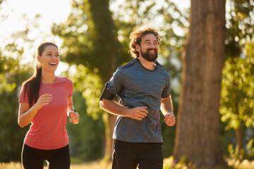 Fototapeta premium Two individuals are jogging side by side in a sunny park, enjoying a recreational activity that enhances their fitness and overall well-being.