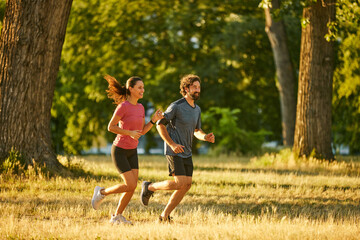Two runners experience the joy of exercise while jogging side by side in a green park during the...