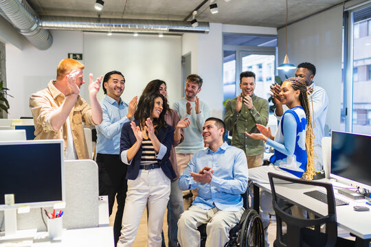 Coworkers clapping, celebrating a goal achievement or good news in a modern office, showing teamwork and inclusion