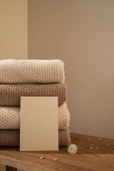 Stack of towels in neutral colors and paper blank in modern aesthetic interior. Fabric bathroom accessories for hygiene, spa and skin care.