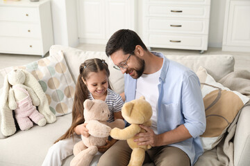 Father and his daughter playing with teddy bears on sofa at home