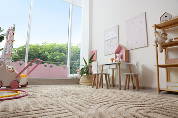 Stylish playroom with toys, furniture and big window, low angle view. Interior design