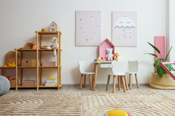 Contemporary furniture, toys and decor near white wall in stylish playroom. Interior design