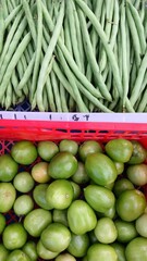 Fresh green beans (Phaseolus vulgaris L) and green tomatoes (Solanum lycopersicum) in plastic boxes sell at traditional market.