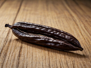 Dark brown carob pods on weathered wood food ingredient