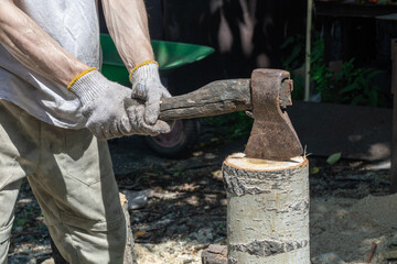 A man using an axe to chop wood on a tree stump in a natural outdoor setting.