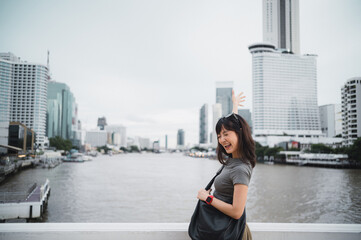 Fototapeta premium Happy young southeast asian woman teenager blogger with smartphone on solo world travel for local cultural experience. Explorer on Chao Phraya river in Bangkok Thailand Asia tourism concept