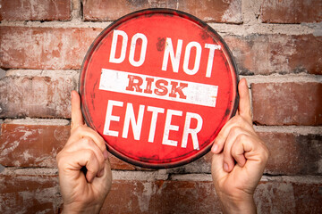Red Circular Warning Sign with Text “Do Not Risk Enter” Held Against Brick Wall
